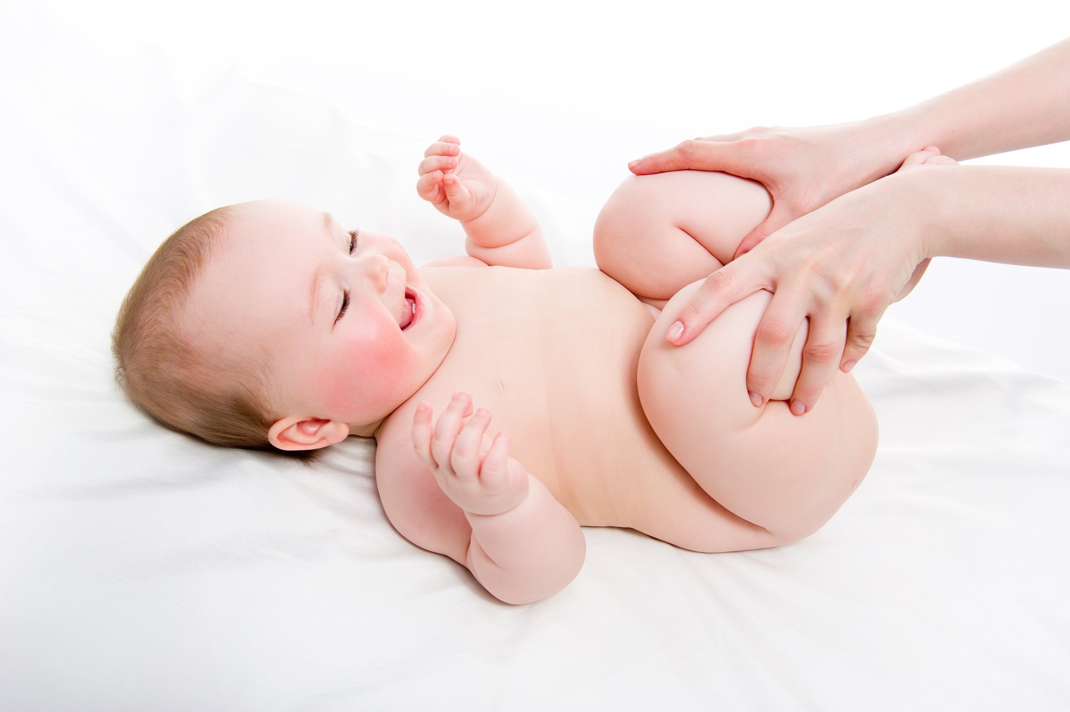 Mother massaging baby's legs on white sheet